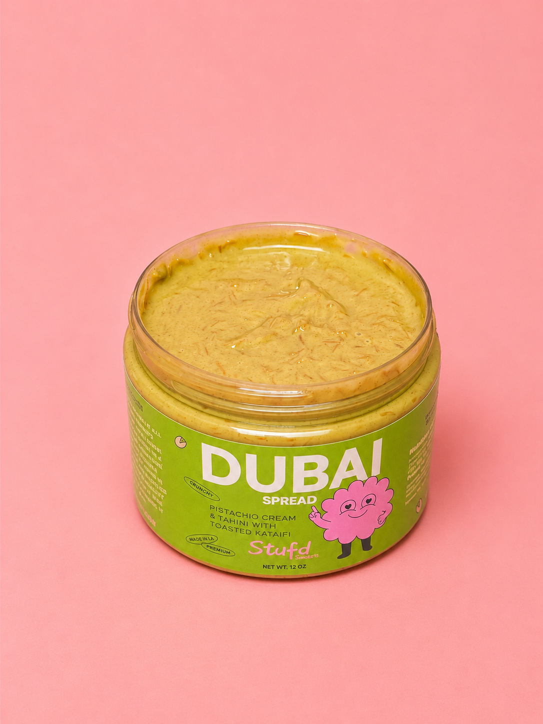 An open jar of Dubai Spread centered on a solid pink background.